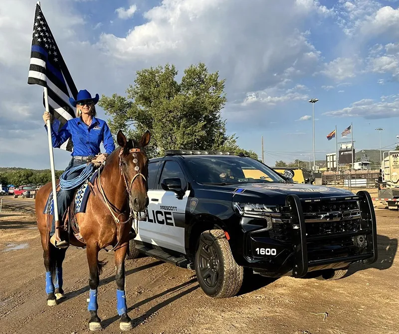 Woman on horse with flag and police vehicle.